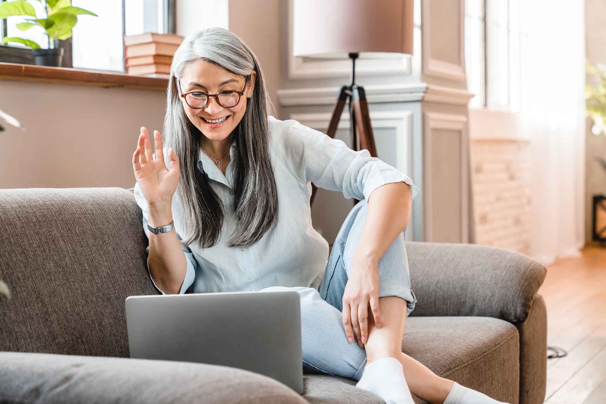 A middle aged woman smiles and waves at her virtual assistant over Zoom