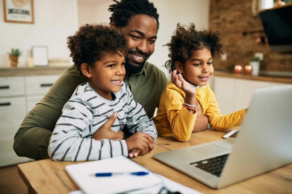 A virtual assistant and father of two with two kids on his knee while attending a Zoom meeting